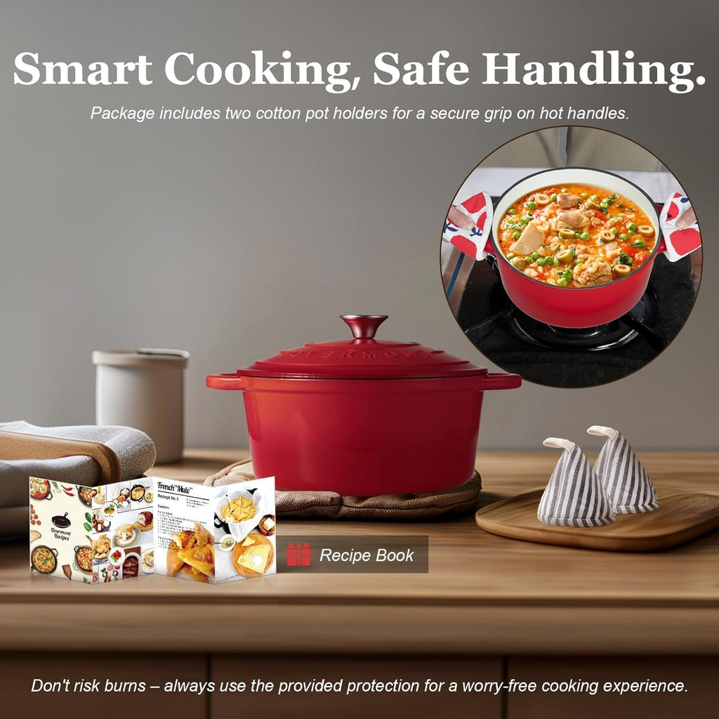 Red cast iron pot with accessories on a wooden surface, including a recipe book and pot holders.